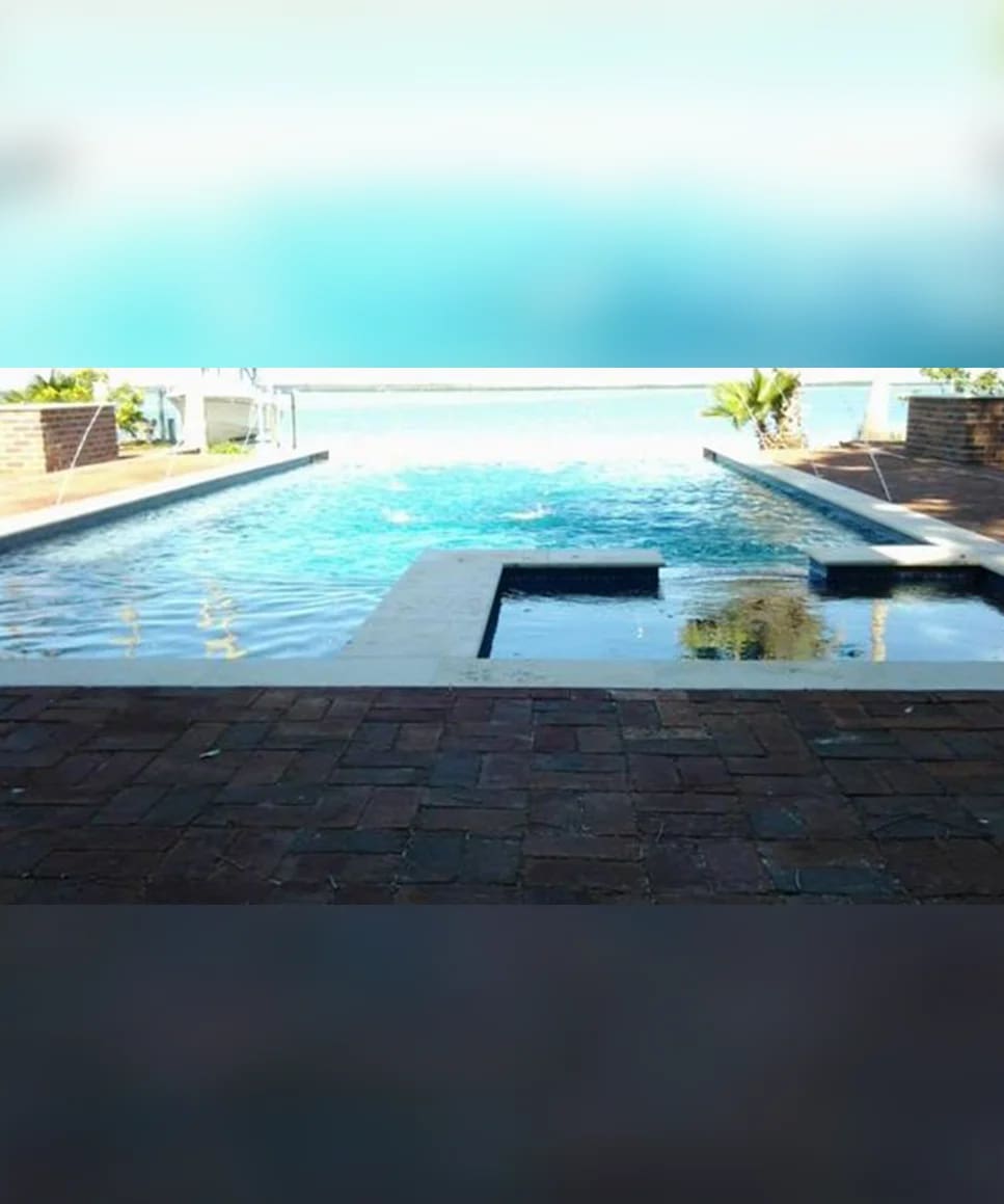 A pool with a view of the ocean and a beach.